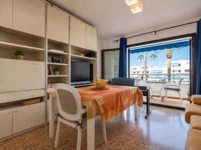 Heller Wohn-Essbereich mit Esstisch und integrierter Medieneinheit, der sich zu einer Terrasse mit Palmenblick und weißen Gebäuden öffnet.