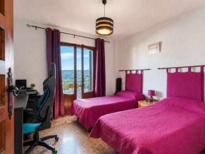 Helles Schlafzimmer mit zwei Einzelbetten, fuchsiafarbenen Kopfteilen und direktem Balkonzugang mit Bergblick. Ein Schreibtischbereich und Terrazzoboden sind vorhanden.