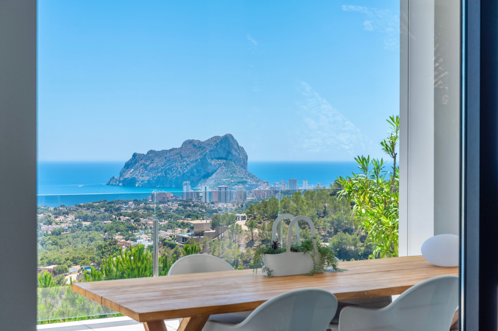 Essbereich im Freien mit Holztisch und modernen weißen Stühlen, der einen Panoramablick auf den Peñon de Ifach, das Mittelmeer und die Küste von Calpe bietet. Essbereich im Freien mit Holztisch und modernen weißen Stühlen, der einen Panoramablick auf den Peñon de Ifach, das Mittelmeer und die Küste von Calpe bietet.