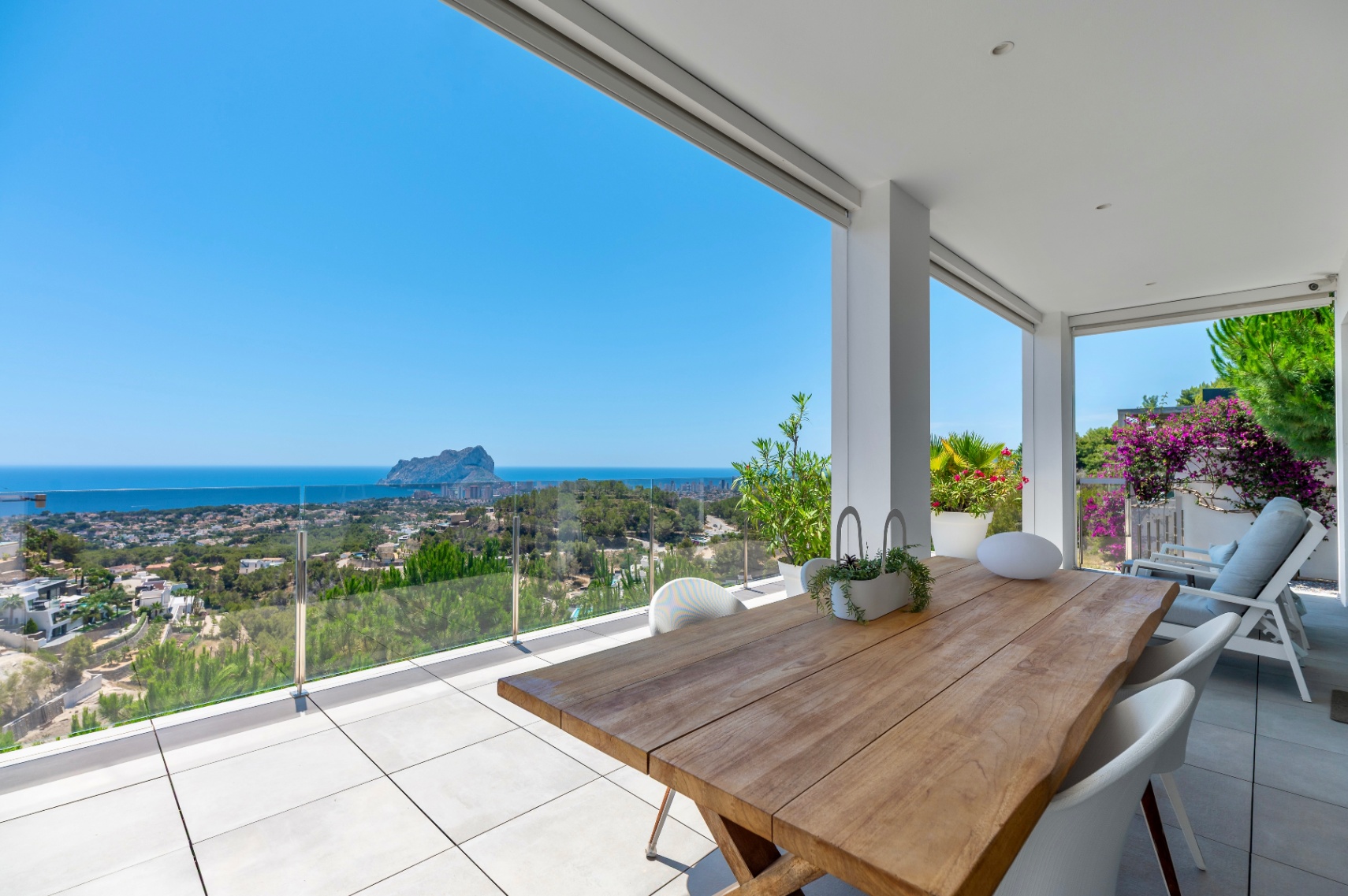 Großzügige überdachte Terrasse mit einem Massivholztisch und weißen Stühlen. Bietet Panoramablick auf das Meer, Calpe und den Peñón de Ifach durch eine Glasbrüstung. Großzügige überdachte Terrasse mit einem Massivholztisch und weißen Stühlen. Bietet Panoramablick auf das Meer, Calpe und den Peñón de Ifach durch eine Glasbrüstung.
