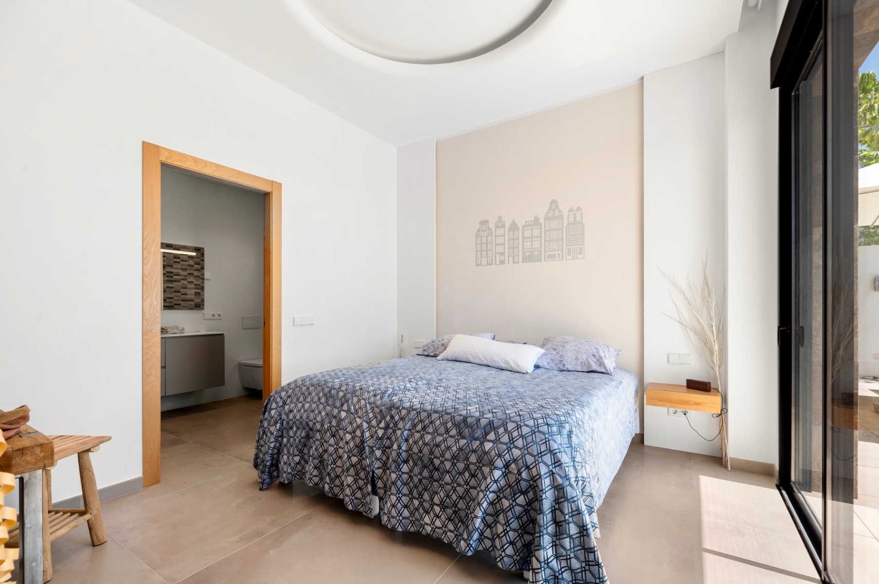 Helles Schlafzimmer mit Doppelbett und einer Akzentwand, verziert mit Gebäudesilhouetten. Es bietet Zugang zu einem En-Suite-Badezimmer und direkten Terrassenzugang durch eine Glasschiebetür. Helles Schlafzimmer mit Doppelbett und einer Akzentwand, verziert mit Gebäudesilhouetten. Es bietet Zugang zu einem En-Suite-Badezimmer und direkten Terrassenzugang durch eine Glasschiebetür.