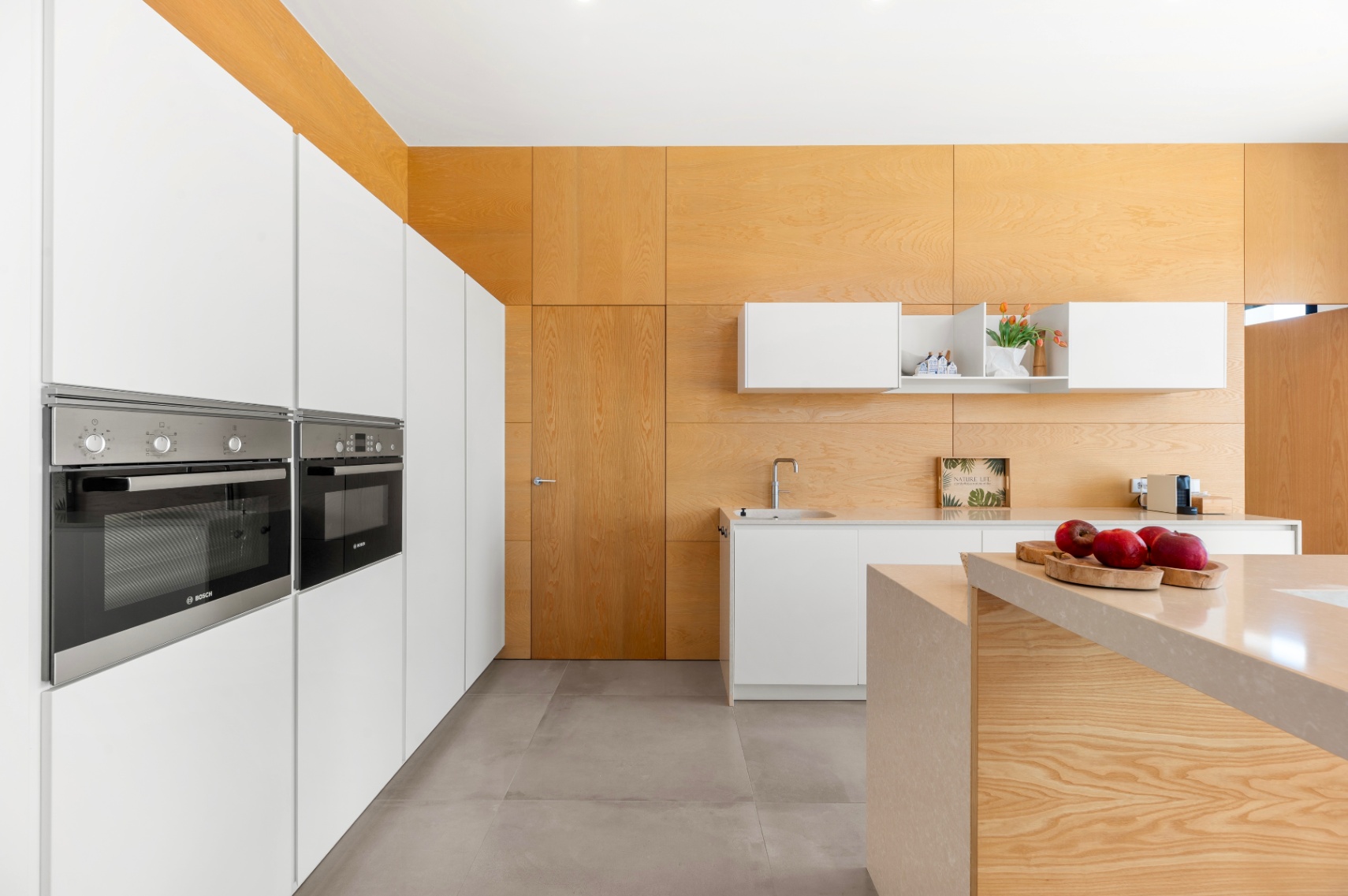 Moderne Küche mit integrierten weißen Schränken und Bosch-Öfen. Eine zentrale Insel mit heller Steinarbeitsplatte und helle Holzverkleidungen an Wänden und Decke prägen den Raum. Moderne Küche mit integrierten weißen Schränken und Bosch-Öfen. Eine zentrale Insel mit heller Steinarbeitsplatte und helle Holzverkleidungen an Wänden und Decke prägen den Raum.