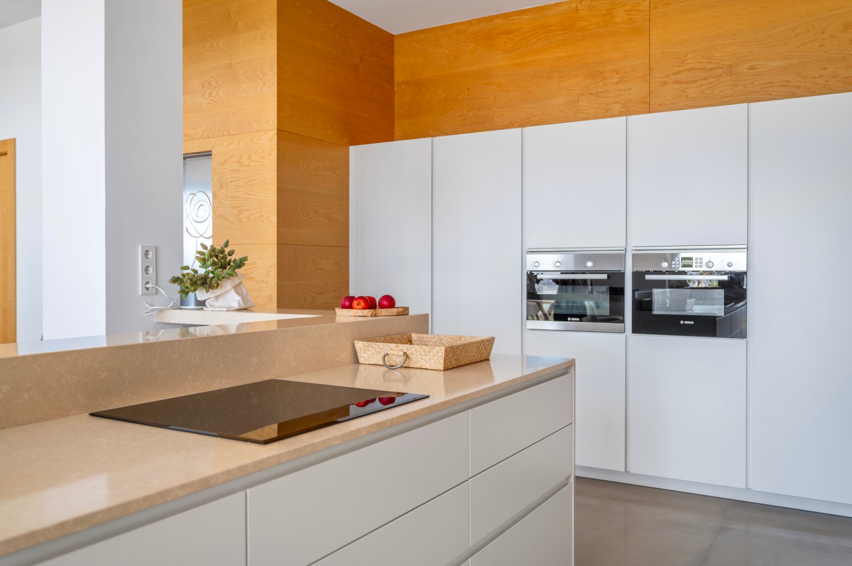 Moderne Küche mit sandfarbener Arbeitsplatte und integriertem Induktionskochfeld. Weiße grifflose Schränke und zwei eingebaute Bosch-Öfen sind sichtbar. Moderne Küche mit sandfarbener Arbeitsplatte und integriertem Induktionskochfeld. Weiße grifflose Schränke und zwei eingebaute Bosch-Öfen sind sichtbar.