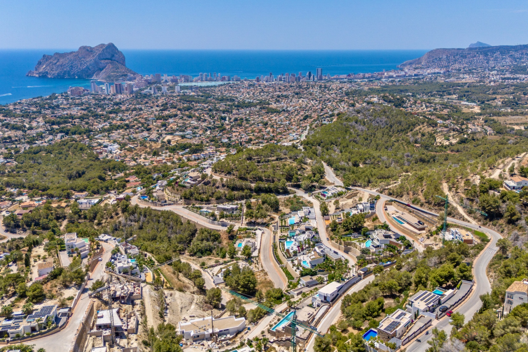 Panoramische Luftaufnahme von Calpe, mit dem Peñon de Ifach, der Küste und einem Wohngebiet mit Villen und Pools in grünen Hügeln und Serpentinenstraßen. Panoramische Luftaufnahme von Calpe, mit dem Peñon de Ifach, der Küste und einem Wohngebiet mit Villen und Pools in grünen Hügeln und Serpentinenstraßen.