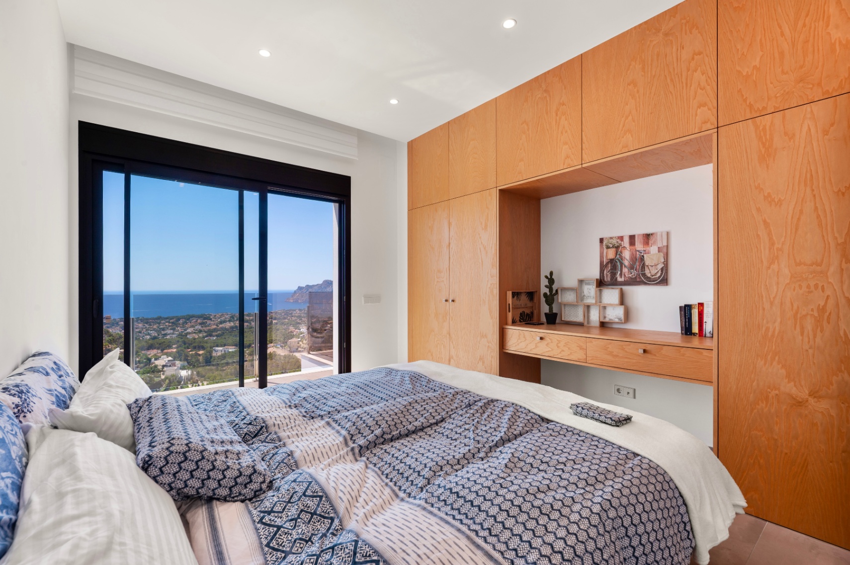 Schlafzimmer mit großen Glasschiebetüren und Panoramablick auf das Meer und die Küste. Maßgefertigte helle Holzschränke mit integriertem Schreibtisch. Schlafzimmer mit großen Glasschiebetüren und Panoramablick auf das Meer und die Küste. Maßgefertigte helle Holzschränke mit integriertem Schreibtisch.