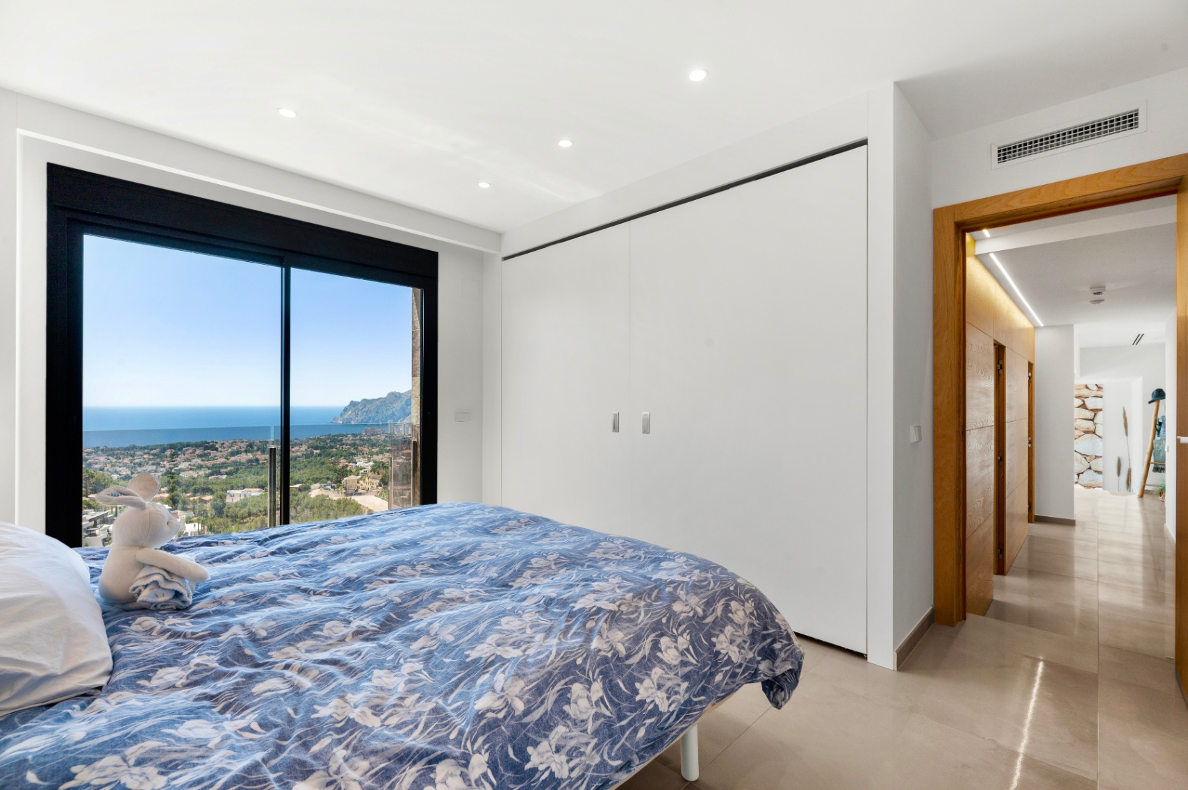 Schlafzimmer mit raumhohen Glasschiebetüren und Panoramablick auf Meer und Stadt. Ausgestattet mit integrierten weißen Kleiderschränken und hellem Fliesenboden. Schlafzimmer mit raumhohen Glasschiebetüren und Panoramablick auf Meer und Stadt. Ausgestattet mit integrierten weißen Kleiderschränken und hellem Fliesenboden.