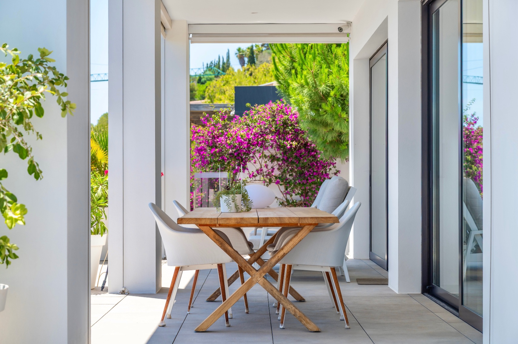 Überdachte Außenterrasse mit Holzesstisch und weißen Stühlen, umgeben von üppigem Grün und leuchtenden Bougainvillea, perfekt für Mahlzeiten im Freien. Überdachte Außenterrasse mit Holzesstisch und weißen Stühlen, umgeben von üppigem Grün und leuchtenden Bougainvillea, perfekt für Mahlzeiten im Freien.