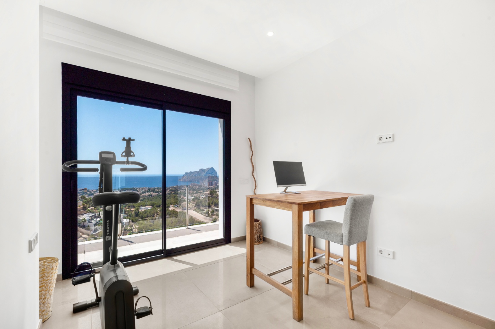 Vielseitiger Raum mit hohem Holzschreibtisch und Heimtrainer, beide mit Blick auf das Meer und den Peñon de Ifach durch die großen Glasschiebetüren. Vielseitiger Raum mit hohem Holzschreibtisch und Heimtrainer, beide mit Blick auf das Meer und den Peñon de Ifach durch die großen Glasschiebetüren.
