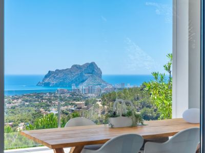 Essbereich im Freien mit Holztisch und modernen weißen Stühlen, der einen Panoramablick auf den Peñon de Ifach, das Mittelmeer und die Küste von Calpe bietet.