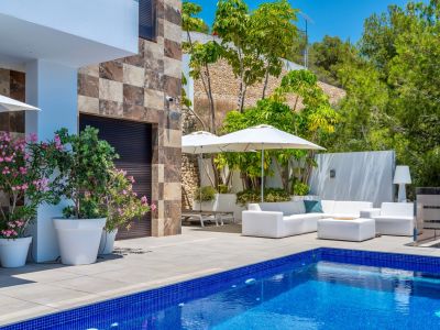 Geräumige Terrasse mit blauem Mosaikpool und weißen Gartenmöbeln unter Sonnenschirmen, ergänzt durch eine Steinfassade und üppige mediterrane Bepflanzung.