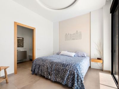 Helles Schlafzimmer mit Doppelbett und einer Akzentwand, verziert mit Gebäudesilhouetten. Es bietet Zugang zu einem En-Suite-Badezimmer und direkten Terrassenzugang durch eine Glasschiebetür.
