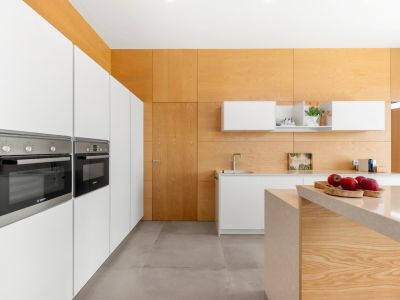 Moderne Küche mit integrierten weißen Schränken und Bosch-Öfen. Eine zentrale Insel mit heller Steinarbeitsplatte und helle Holzverkleidungen an Wänden und Decke prägen den Raum.