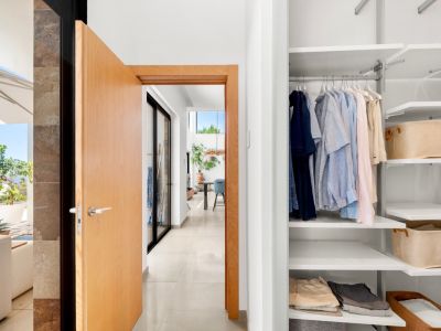 Moderner Flureingang mit offener heller Holztür, der einen weißen Einbauschrank mit verstellbaren Regalen und einen sonnigen Terrassenbereich mit Meerblick zeigt.