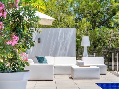 Moderner Outdoor-Loungebereich mit weißen Modulsofas und passendem Ottoman auf einer gefliesten Terrasse. Umgeben von üppigem Grün und einer Glasbrüstung neben dem Pool.