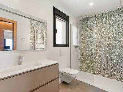 Modernes Badezimmer mit ebenerdiger Dusche und Mosaikwand in Erdtönen. Es verfügt über einen schwebenden Waschtisch mit integriertem Waschbecken, ein Wand-WC und ein schwarz gerahmtes Fenster.