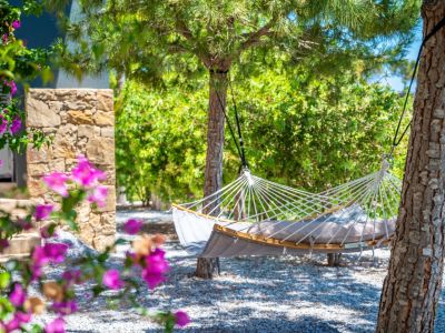 Ruhiger Gartenbereich mit einer bequemen grauen Hängematte mit Holzspreizstäben, zwischen Bäumen auf einem Kiesbett, umrahmt von lebhaften Bougainvilleen.