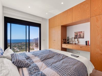 Schlafzimmer mit großen Glasschiebetüren und Panoramablick auf das Meer und die Küste. Maßgefertigte helle Holzschränke mit integriertem Schreibtisch.