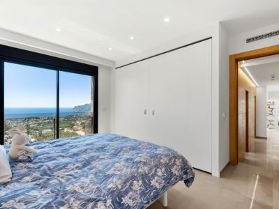 Schlafzimmer mit raumhohen Glasschiebetüren und Panoramablick auf Meer und Stadt. Ausgestattet mit integrierten weißen Kleiderschränken und hellem Fliesenboden.