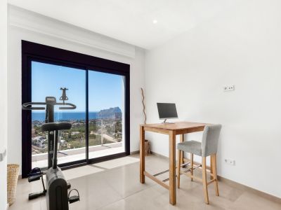 Vielseitiger Raum mit hohem Holzschreibtisch und Heimtrainer, beide mit Blick auf das Meer und den Peñon de Ifach durch die großen Glasschiebetüren.