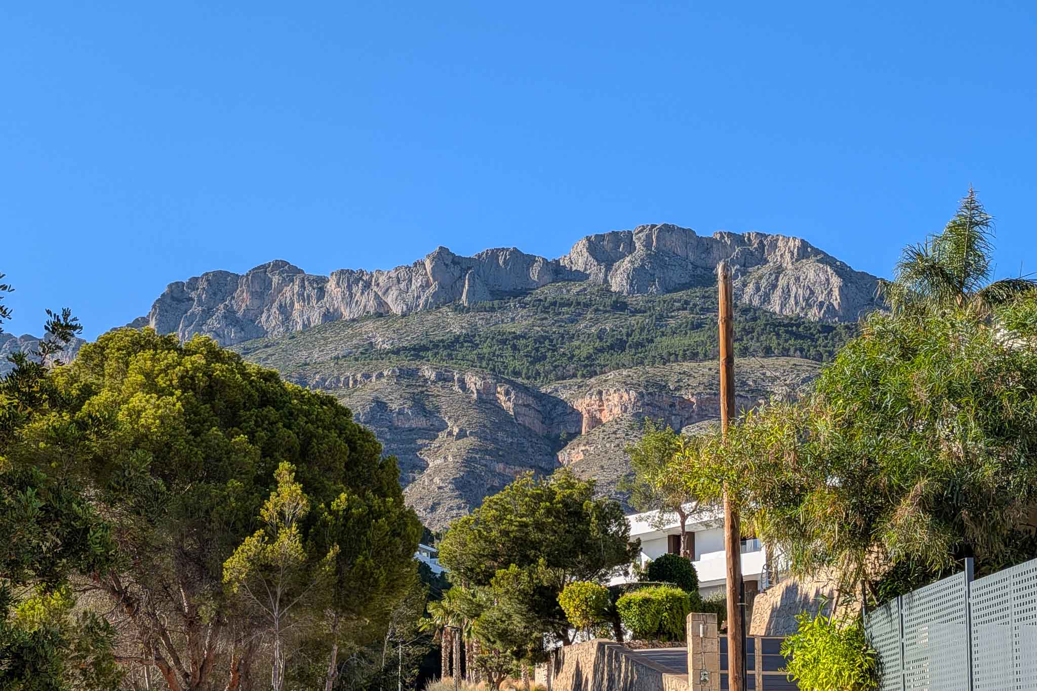 Blick auf die majestätische Sierra de Bernia, mit ihren felsigen Gipfeln und grünen Hängen, umrahmt von der üppigen mediterranen Vegetation des Anwesens.