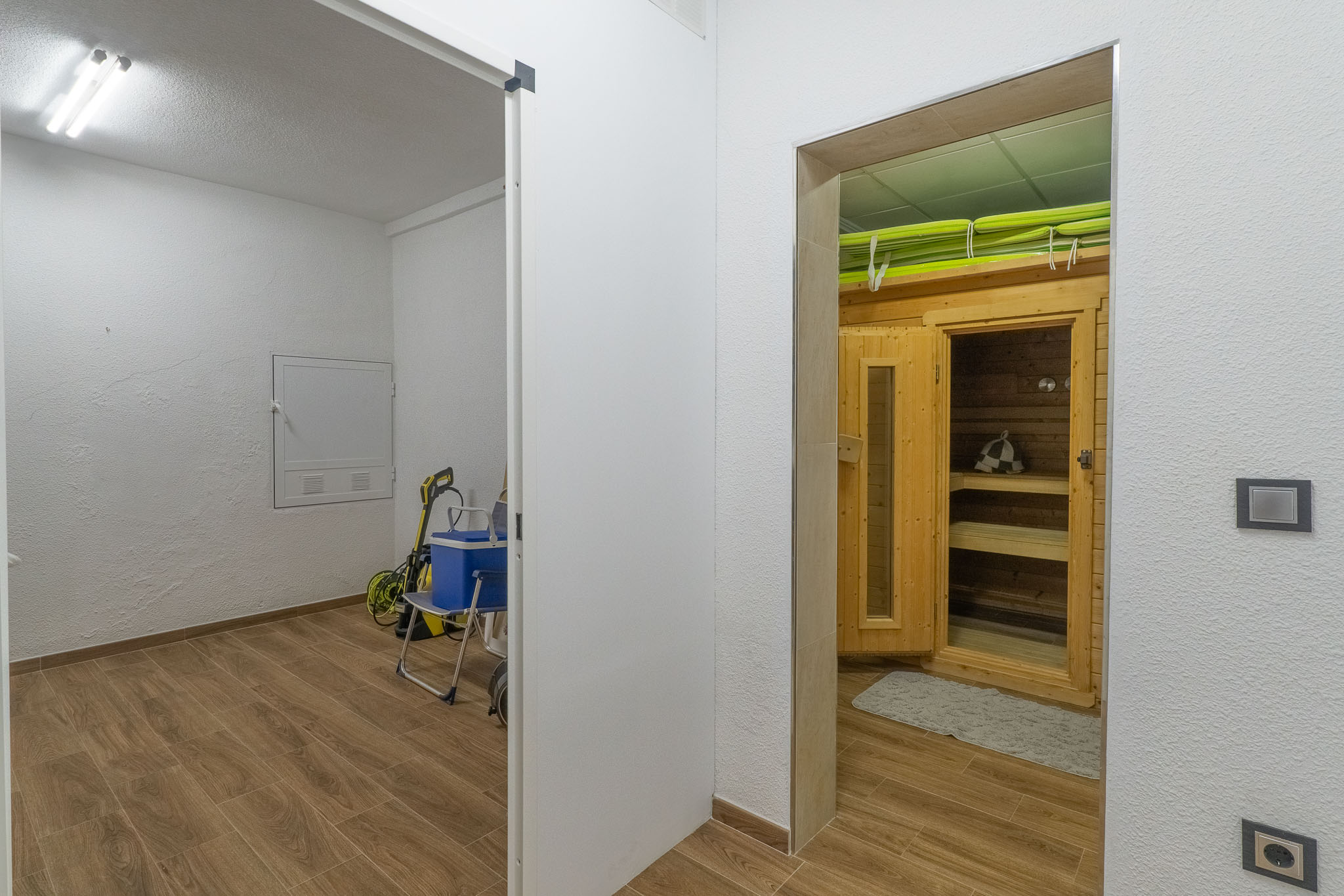 Eigener Wellnessbereich mit Holzkabine und Sitzbänken, angrenzend an einen praktischen Hauswirtschaftsraum. Beide Bereiche haben einen Holzoptik-Fliesenboden.