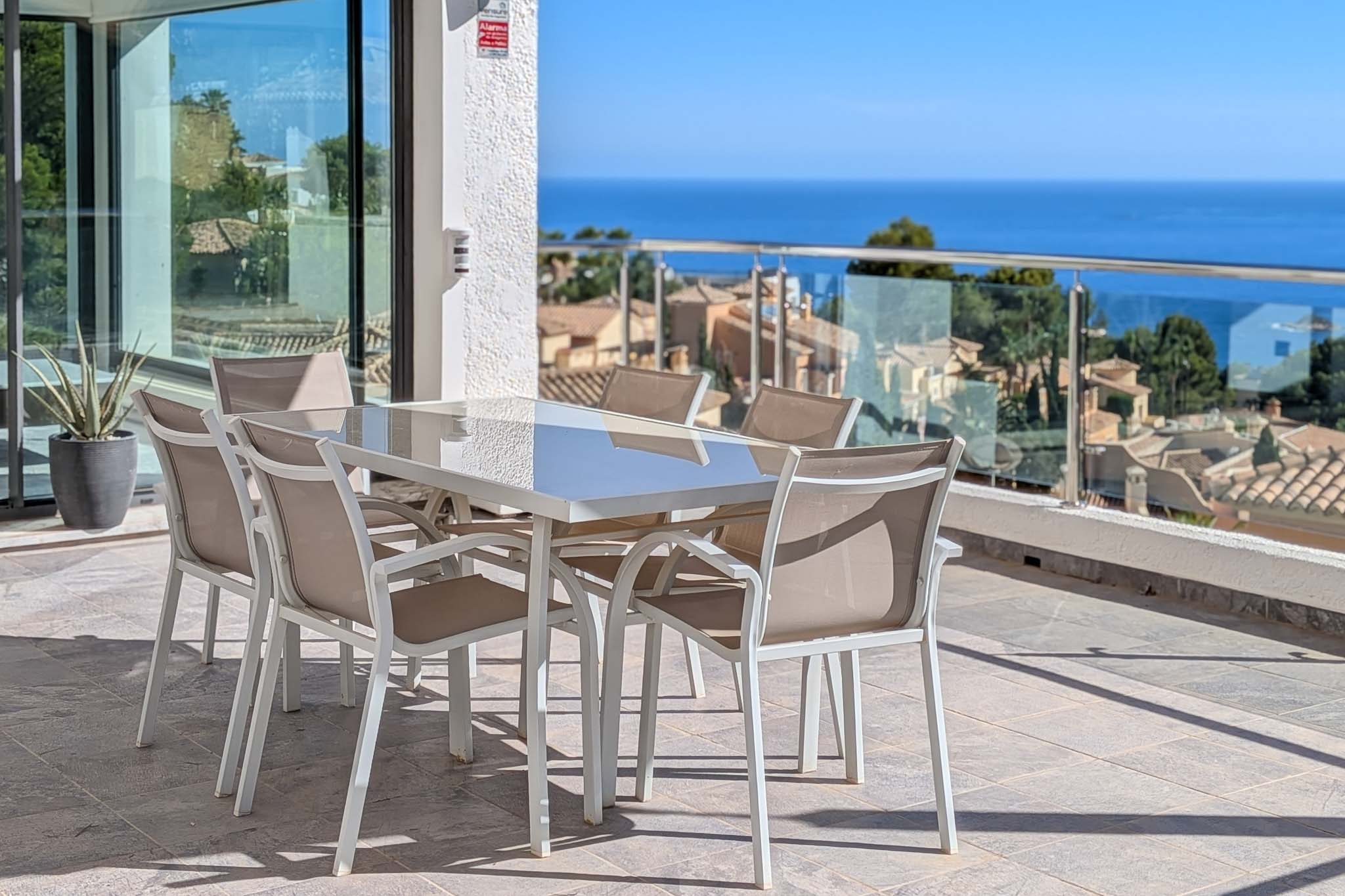 Geräumige Außenterrasse mit Esstisch und Stühlen, die einen Panoramablick auf das Mittelmeer und die Dächer von Altea Hills bietet. Glasschiebetüren verbinden den Innenbereich.