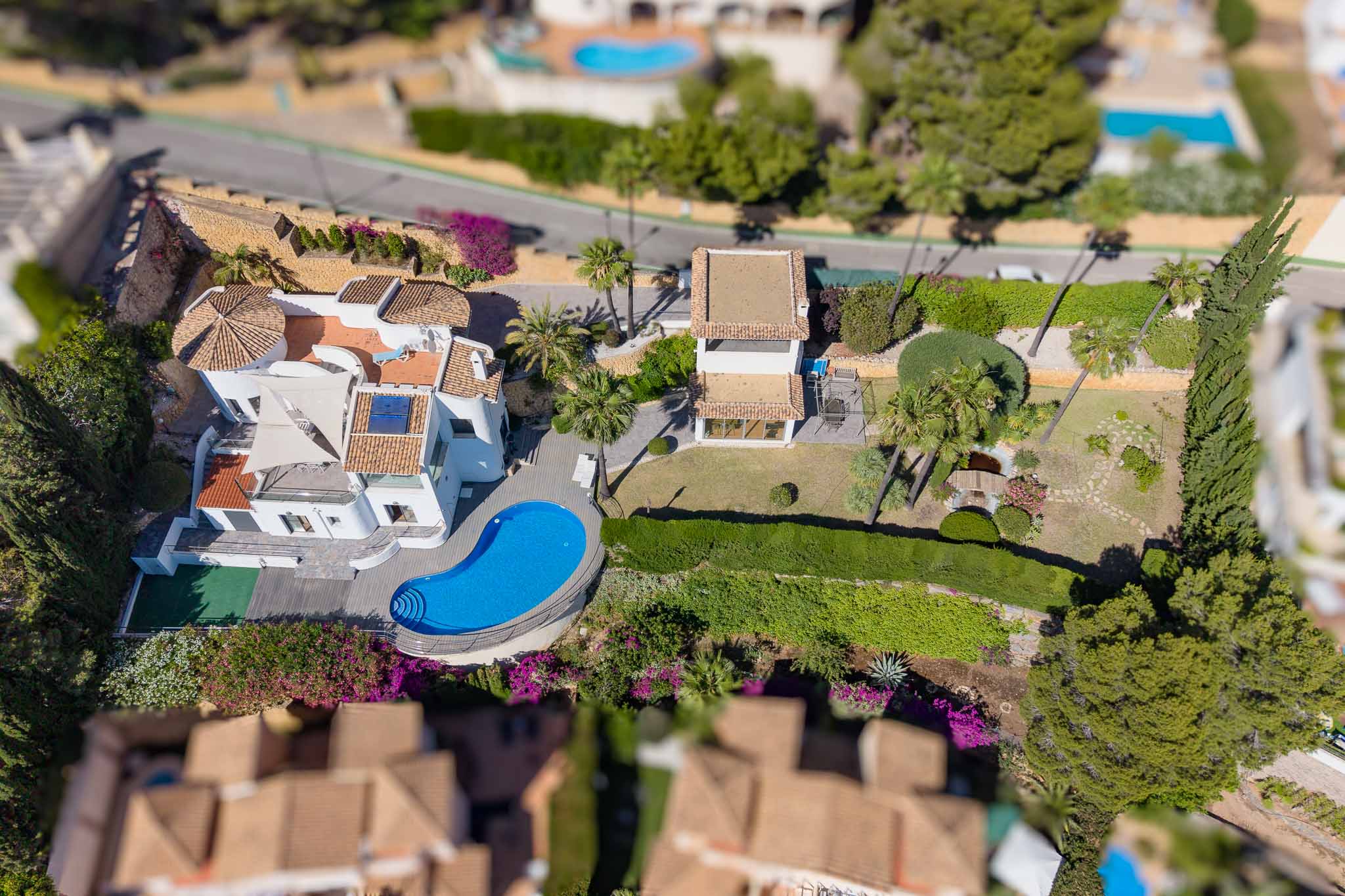Luftaufnahme der Villa mit unregelmäßig geformtem Pool, weitläufigen flachen Gärten mit Teich und einem separaten Nebengebäude. Traditionelle Ziegeldächer und mediterrane Vegetation prägen das Bild.