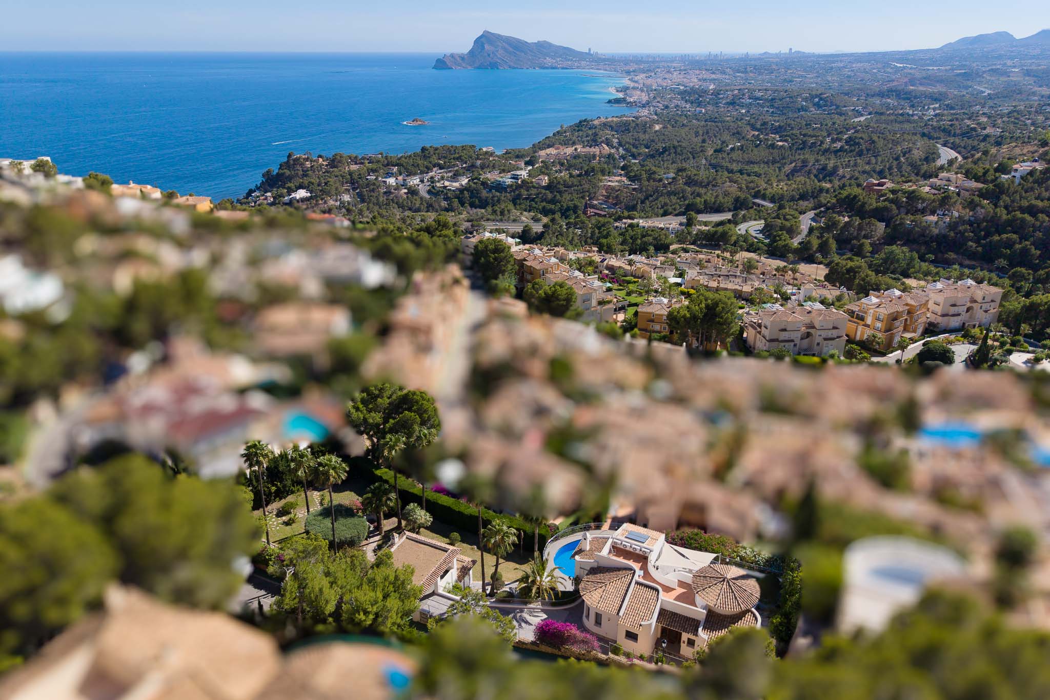 Luftaufnahme einer Villa in Altea Hills mit geschwungenem Pool, Terrakottadächern und üppigen Gärten, vor der Kulisse des Mittelmeers und der Küste.