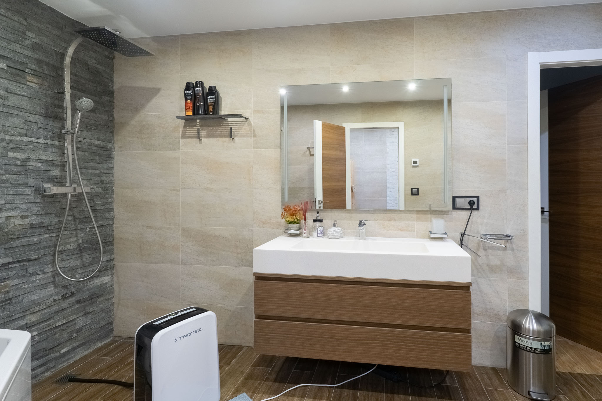 Modernes Badezimmer mit Regendusche und Schiefer-Akzentwand, schwebendem Holzwaschtisch und integriertem Waschbecken. Fliesen in Holzoptik.
