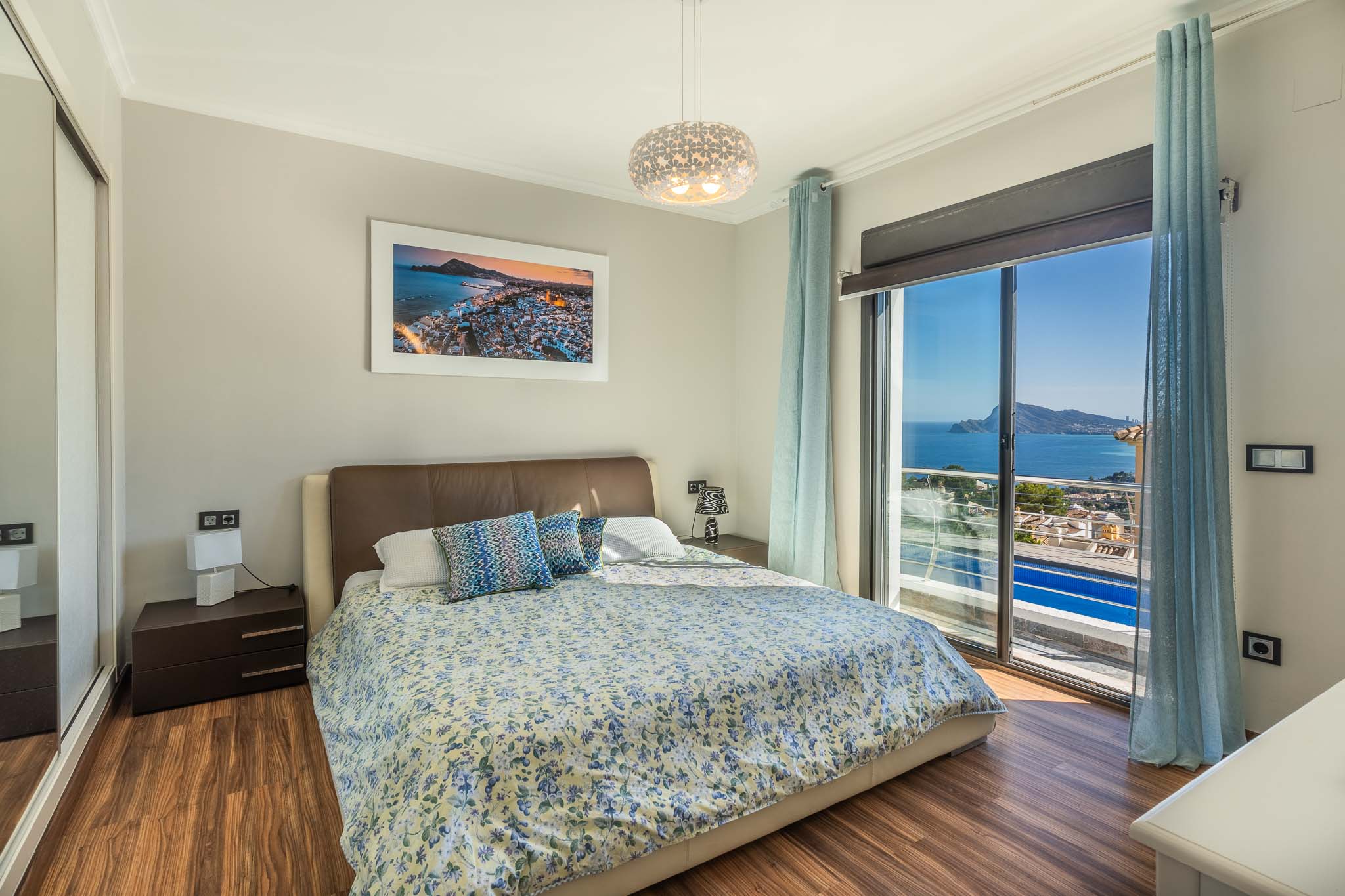 Schlafzimmer mit Doppelbett, Holzlaminatboden und weitem Meerblick durch die große Glasschiebetür. Ein Spiegelschrank ist ebenfalls vorhanden.