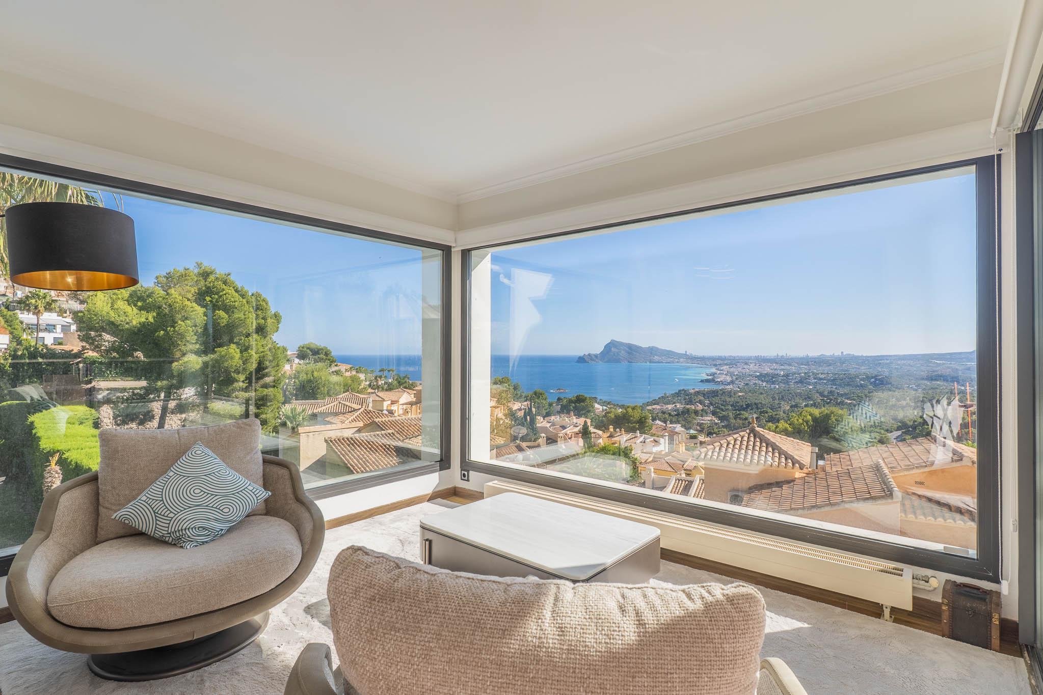 Wohnbereich mit großen Eckfenstern, die einen Panoramablick auf das Meer und die Küste freigeben. Zwei Sessel und ein moderner Couchtisch gestalten diesen hellen Raum.