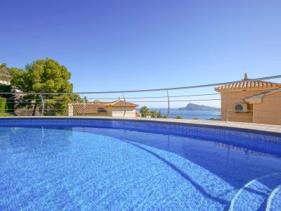 Blauer Mosaik-Swimmingpool mit integrierten Stufen und modernem Geländer, der einen Panoramablick auf das Meer, traditionelle Dächer und die Küste bietet.