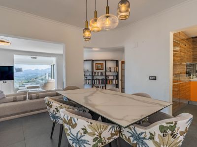 Design-Essbereich mit Marmor-Effekt-Tisch und gemusterten Stühlen, beleuchtet von modernen Pendelleuchten. Verbindet sich mit dem Wohnzimmer und bietet Panoramablicke auf die Berge.
