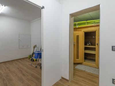 Eigener Wellnessbereich mit Holzkabine und Sitzbänken, angrenzend an einen praktischen Hauswirtschaftsraum. Beide Bereiche haben einen Holzoptik-Fliesenboden.