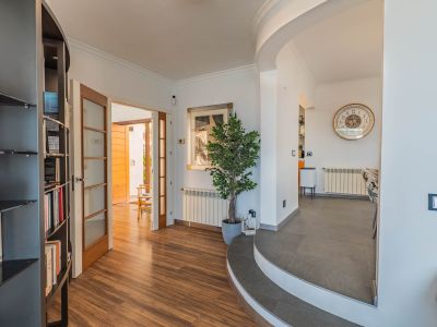 Eingangsbereich mit Holzlaminatboden, der durch Glastüren zu einem Außenbereich führt. Geschwungene geflieste Stufen verbinden den Essbereich, ergänzt durch ein integriertes Bücherregal.