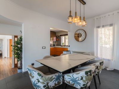Essbereich mit Marmor-Effekt-Tisch und Stühlen mit tropischem Muster. Moderne Hängeleuchten erhellen den Raum, der sich zu einer Küche mit orangefarbenen Schränken öffnet.
