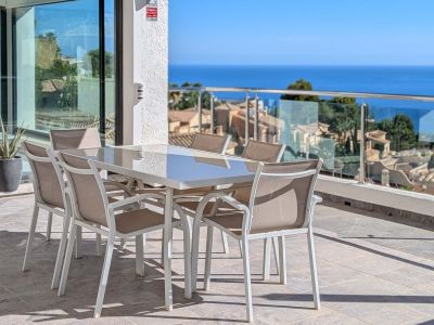 Geräumige Außenterrasse mit Esstisch und Stühlen, die einen Panoramablick auf das Mittelmeer und die Dächer von Altea Hills bietet. Glasschiebetüren verbinden den Innenbereich.
