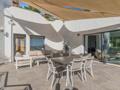 Geräumige Außenterrasse mit Fliesenboden, Essgruppe und Loungebereich unter einem ausziehbaren Sonnensegel. Große Glasschiebetüren verbinden zum Innenraum.