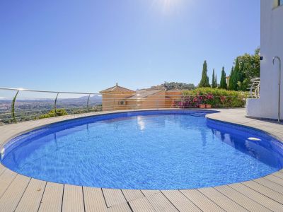 Geschwungener Pool mit blauen Mosaikfliesen und heller Holzterrasse, umgeben von einem Edelstahlgeländer, mit Panoramablick auf Tal und ferne Stadt.