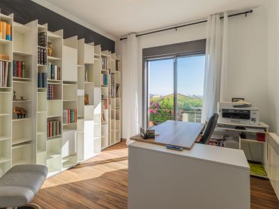 Helles Arbeitszimmer mit weißem modularem Bücherregal, Holzboden und modernem Schreibtisch vor einem Balkon mit üppiger Gartenansicht. Natürliches Licht durchflutet den Raum.