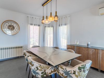 Helles Esszimmer mit Marmoreffekt-Tisch, Stühlen mit tropischem Muster und einer modernen linearen Hängeleuchte, von Tageslicht erhellt.