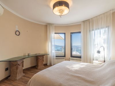 Helles Schlafzimmer mit Panoramameerblick durch große Fenster mit Vorhängen und einem einzigartigen Glastisch auf geschnitzten Holzsockeln.
