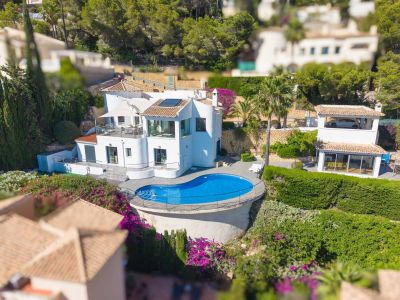Luftaufnahme der weißen Villa, mit einem einzigartigen nierenförmigen Pool, umgeben von einer Holzterrasse und Metallgeländer. Mehrere Terrassen und üppige mediterrane Gärten sind sichtbar.