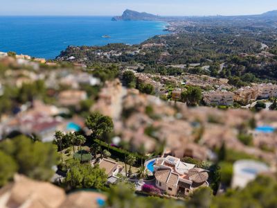 Luftaufnahme einer Villa in Altea Hills mit geschwungenem Pool, Terrakottadächern und üppigen Gärten, vor der Kulisse des Mittelmeers und der Küste.