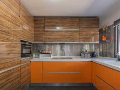 Moderne Küche mit glänzenden Holzmaser-Oberschränken und leuchtend orangefarbenen Unterschränken, ergänzt durch helle Arbeitsplatten und einen metallischen Mosaik-Spritzschutz.