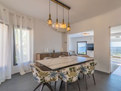 Moderner Essbereich mit Marmortisch und Stühlen im Tropenmuster. Eine lineare Pendelleuchte beleuchtet den Raum, der durch angrenzende Zimmer Meerblick bietet.