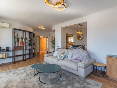 Moderner Wohnbereich mit hellem Sofa, zwei runden Teetischen in Petrol und einem großen modularen Bücherregal. Design-Deckenleuchten erhellen den Raum.