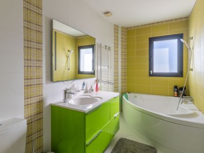 Modernes Badezimmer mit Eckbadewanne und leuchtend grünem Waschtisch. Wände gefliest mit weißen Struktur-, lindgrünen und karierten Mosaikfliesen. Mit Fenster und Handtuchheizkörper.