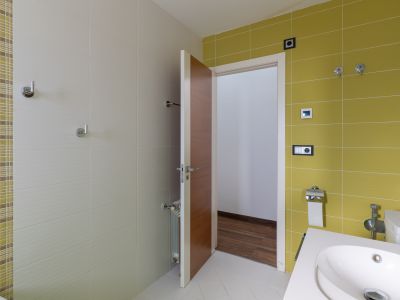 Modernes Badezimmer mit Wandfliesen in Limettengrün und strukturiertem Beige, ergänzt durch ein Mosaikband. Ausgestattet mit einem zeitgemäßen Waschbecken und einer Holztür.