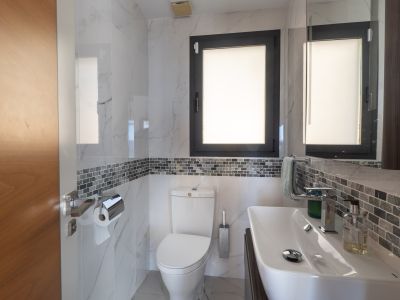 Modernes Badezimmer mit weißen Marmor-Effektfliesen, einem grauen Mosaikband und einem dunkel gerahmten Fenster. Mit elegantem weißen Waschbecken und passender Toilette.